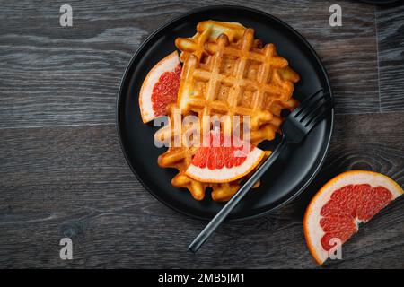 Waffeln und Grapefruit auf einem schwarzen Teller auf einem Holztisch Stockfoto