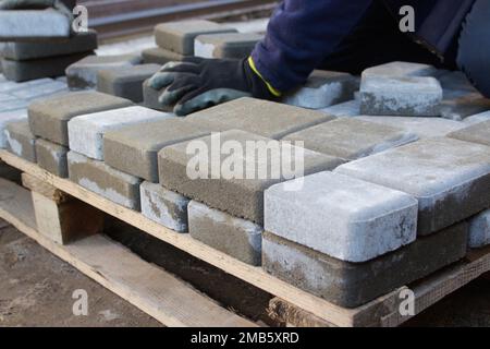 Meister des Defokussierungsfertigers. Der Mensch legt Pflastersteine in Schichten. Gartenziegel Weg Pflaster von professionellen Arbeiter. Hände des Arbeiters, der Betonfertiger installiert Stockfoto