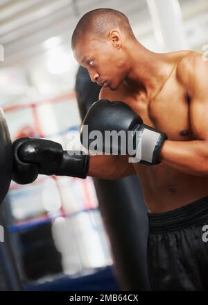 Den Schlagball zu zerschlagen. Ein afroamerikanischer Boxer, der mit einem Boxsack im Fitnessstudio trainiert. Stockfoto