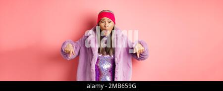Mode- und Shopping-Konzept. Beeindruckt asiatische weibliche Zeigefinger nach unten und Blick aufgeregt bei der Kamera, zeigt genial promo Angebot, stehen über Stockfoto