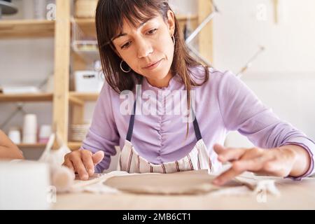 Töpferin mit Schürze, die Tonplatten in einer Töpferwerkstatt zubereitet. Handwerk, Kunst und Hobbys. Stockfoto