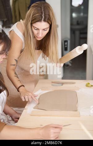 Freunde mit Schürzen in einer Töpferwerkstatt bereiten Ton vor, um Stücke zu kreieren. Handwerksklasse. Stockfoto