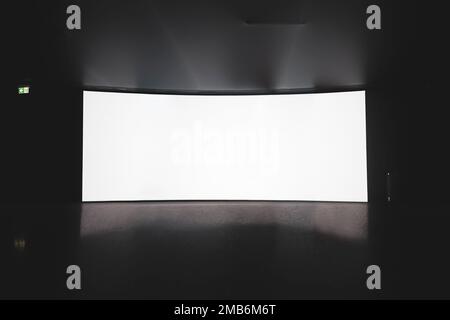 Kino. Ein leerer weißer Kinoleinwand auf einem Ständer im Saal im Dunkeln. Stockfoto