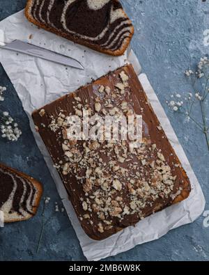 Ein vertikaler Blick von oben auf Marmorkuchen mit Schokolade und Nüssen auf blauer Oberfläche, dekoriert mit weißen Wildblumen Stockfoto