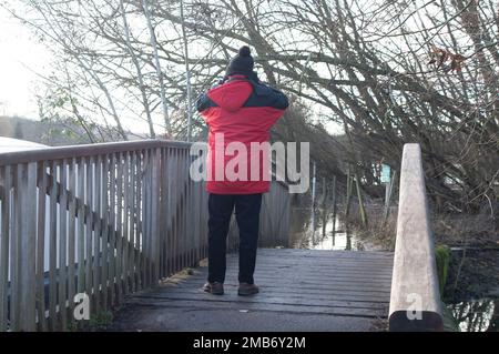 Marlow, Buckinghamshire, Großbritannien. 20. Januar 2023. Ein Mann schaut auf den überfluteten Themspfad. Die Themse in Marlow ist nach starkem Regen Anfang Januar am Ufer geplatzt. Der Wasserstand sinkt, aber es gibt Eis auf dem Themsenpfad, wo das Wasser gefroren ist. Die Wasserstände befinden sich jetzt an einigen Stellen auf derselben Höhe wie der Pfad. Für die Themse von Hurley bis Cookham, einschließlich Marlow, ist weiterhin eine Hochwasserwarnung aktiv. Kredit: Maureen McLean/Alamy Live News Stockfoto