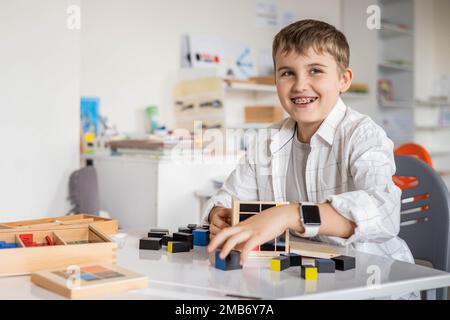 Glücklicher Junge, der Montessori-Stoff-Trinomialwürfel am Klassenschreibtisch zusammenstellt Stockfoto