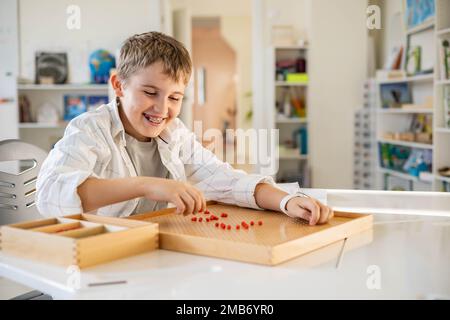 Junge, Kinder, Montessori-Holzbrett mit roten Perlen, Herzform auf dem Schreibtisch Stockfoto