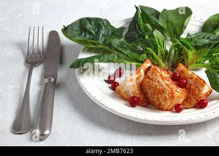Gegrillter Mozzarella halloumi mit grünem Spinat und Preiselbeeren mit Besteck Stockfoto