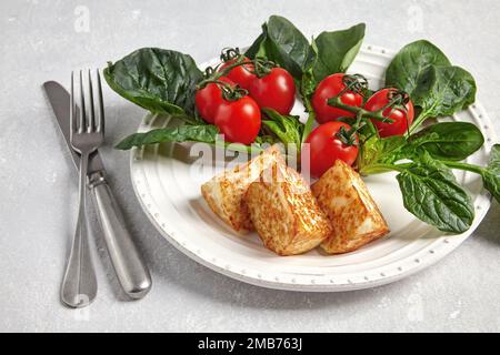 Gebratener Quark Mozzarella halloumi mit grünem Spinat und Kirschtomaten auf einem Zweig mit Besteck Stockfoto