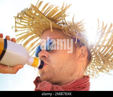 Ich trinke einen Schluck. Ein junger Mann mit Strohhut, der aus einer Flasche trinkt. Stockfoto
