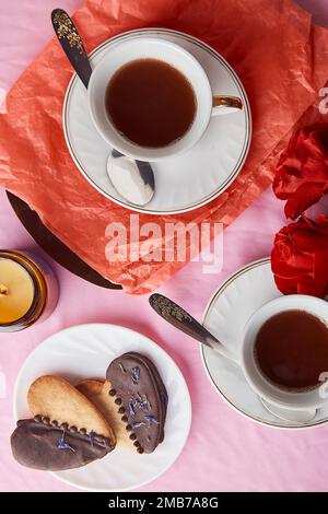 Herzförmige Valentinskekse, Kaffeetassen und rote Rosen. Vegane Kekse mit orangefarbenem Quark. Lagom pinke Ferienwohnung Stockfoto