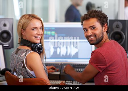 Dein Album ist in guten Händen. Zwei junge Toningenieure sitzen vor einem Mischpult und schauen über ihre Schultern - Porträt. Stockfoto