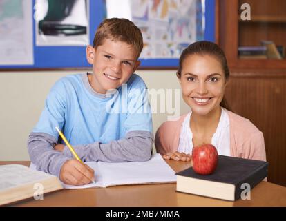 Die Liebe zum Lernen fördern. Ein unterstützender junger Lehrer, der neben ihrem Schüler sitzt, während er in einem Buch schreibt. Stockfoto