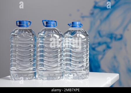 Drei volle 5-Liter-Flaschen Wasser auf einem weißen Tisch. Wasserzufuhr Stockfoto