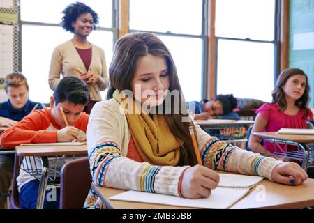 Ausbildung, Schreiben und Prüfung mit Kindern im Klassenzimmer der Hochschule für Akademie, Wissen und Lernen. Studium, Schule und Notizbuch mit Schülern und Stockfoto