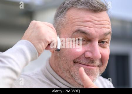 Porträt eines grauhaarigen Schwerhörigen mittleren Alters zwischen 50 und 60 Jahren mit einem Hörgerät im Ohr, das Daumen nach oben gibt Stockfoto