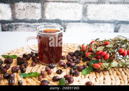 Rosehip-Tee, frisch gebrühter Obst- und Kräutertee, Bio-Rosehips im Hintergrund, Nahaufnahme. Stockfoto