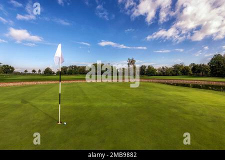 Malerischer Blick auf den Golfplatz mit Fahnennadel und Ball auf grünem Rasen unter blauem Himmel an sonnigen Tagen Stockfoto