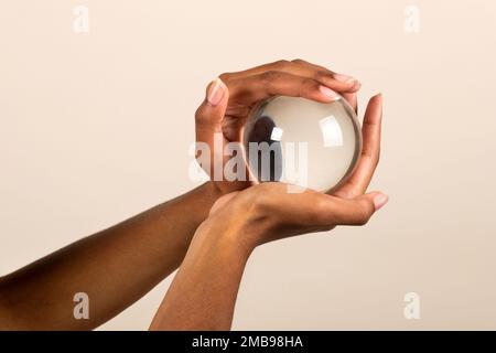 Nahaufnahme einer anonymen afroamerikanischen Frau mit transparenter Glaskugel in den Händen auf pinkfarbenem Hintergrund Stockfoto