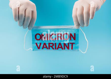 Zugeschnittene Ansicht des Arztes in Latexhandschuhen, die medizinische Maske mit omicron-Variante Beschriftung isoliert auf blauem, Stock Bild Stockfoto