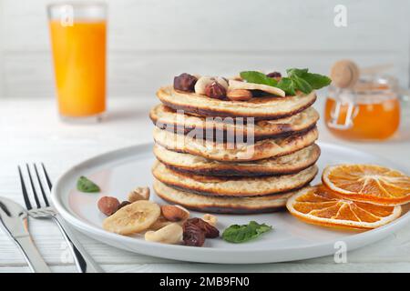 Frische, köstliche Pfannkuchen mit getrockneten Bananen, Orangen, Nüssen und Honig auf einem Teller. Stockfoto