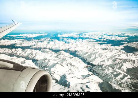 Luftaufnahme der europäischen Alpen mit nebligen Horizont und Teil eines Flugzeugflügelmotors - Reisekonzept und Winterurlaub auf weißen Schneebirgen Stockfoto