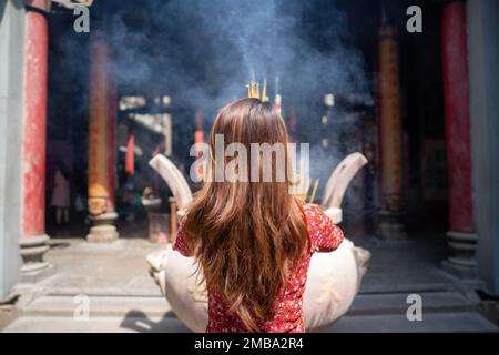 Ein vietnamesisches Mädchen in traditionellem, langem Kleid oder Ao Dai-Kleid betet mit Weihrauch im brennenden Topf einer Pagode in Ho-Chi-Minh-Stadt, Vietnam. T Stockfoto