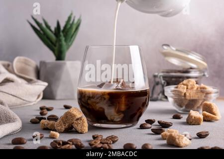 Hausgemachter Eiskaffee. Schwarzer Kaffee mit Eis und Milch oder Sahne im Glas für eine leckere und erfrischende Pause auf grauem Küchenhintergrund Stockfoto