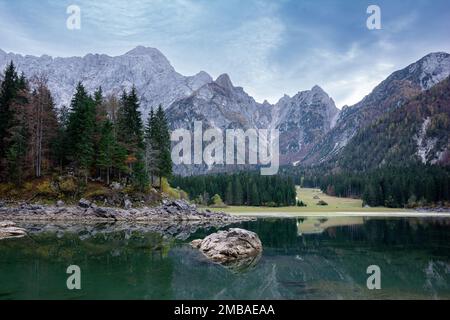 Malerische Landschaft von Lago oder Laghi di Fusine See in Italien mit Fichten am Ufer am blauen Himmel und Gebirgshintergrund Stockfoto