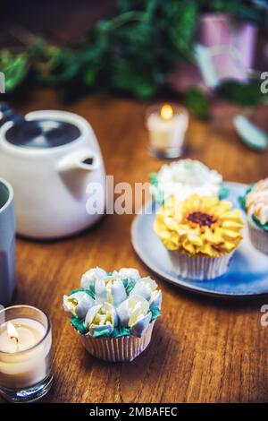 Verschiedene Cupcakes dekoriert mit bunten Blumenglasuren auf Holztisch, Blumenstrauß, Hochzeitstorte, Nachmittagstee, Urlaubskonzept Stockfoto
