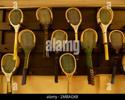 Jesmond Dene Real Tennis Club, Matthew Bank, Jesmond, Newcastle upon Tyne, 2010. Eine Auswahl an Schlägern für echtes Tennis, die an einer Wand vor dem Platz im Jesmond Dene Real Tennis Club, Newcastle upon Tyne hängen. Der Tennisplatz wurde 1894 für Sir Andrew Noble gebaut und wird seit seiner Gründung im Jahr 1932 vom Jesmond Dene Real Tennis Club genutzt. Echtes Tennis unterscheidet sich vom späteren Rasentennis in mehrfacher Hinsicht, einschließlich der Vorkehrungen für Zuschauer, der Konstruktion der Tennisbälle und des Stils und Materials der Schläger. Die Schläger sind oft aus Hickory oder Asche mit engen Schnüren Stockfoto