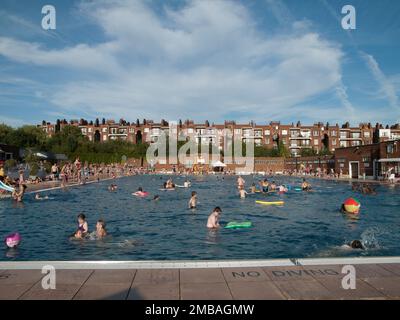 Parliament Hill Fields Lido, Gordon House Road, Gospel Oak, Camden, Greater London Authority, 2012. Das geschäftige Schwimmbad am Parliament Hill Fields Lido in Gospel Oak, vom westlichen Ende aus gesehen, mit dem Hinterkopf der Parliament Hill Mansions, Lissenden Gardens dahinter. Parliament Hill Fields Lido wurde 1938 eröffnet und von Harry Arnold Rowbotham und T L Smithson entworfen. Es war eine von dreizehn Lidos, die zwischen 1909 und 1939 vom London County Council gebaut wurden. Der Pool blieb bis zu einer größeren Renovierung in den Jahren 2004-2005 geöffnet. Originalelemente wie die Hauptuhr, die Beschilderung und der Strahlbrunnen wurden wiederhergestellt Stockfoto