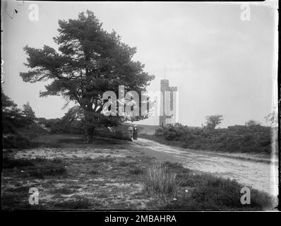 Leith Hill Tower, Leith Hill, Wotton, Mole Valley, Surrey, 1912. Ein Blick auf den Leith Hill in Richtung Leith Hill Tower in der Ferne, wobei ein Paar in der Mitte an einem Baum vorbeigeht. Dieser Torenturm wurde 1764 oder 65 von Richard Hulls vom Leith Hill Place erbaut und befindet sich auf dem Gipfel des Leith Hill, dem zweithöchsten Platz im Südosten Englands. Stockfoto