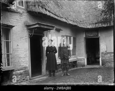 Royal Oak Inn, Wootton Rivers, Wiltshire, 1923. Ein Porträt von Mr. &Amp; Mrs. Gilbert im Innenhof des Royal Oak Inn. Ein Schild über einer der Türen zeigt, dass Willis Gilbert eine Lizenz für den Verkauf von Bier, Wein, Spirituosen und Tabak erhielt, die auf dem Gelände konsumiert werden sollten. Stockfoto