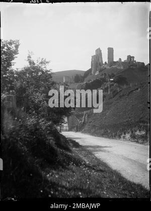 Corfe Castle, Corfe Castle, Purbeck, Dorset, 1927. Blick auf die Ruinen von Corfe Castle von Osten auf der Sandy Hill Lane. Im Negativindex für die Sammlung hat der Fotograf aufgezeichnet, dass das Foto von der Straße zur Challow Farm aufgenommen wurde, und sie bezieht sich auf ein Signal. Ein Bahnsignal ist in der mittleren Entfernung zu sehen, ebenso ein Tor auf der anderen Straßenseite. Stockfoto