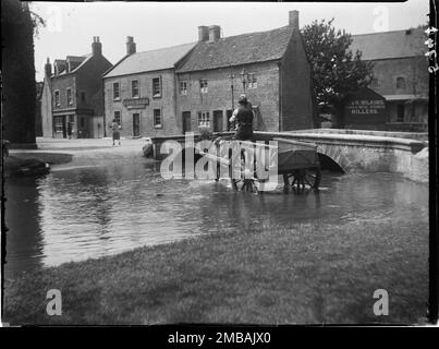 Sherborne Street, Bourton-on-the-Water, Cotswold, Gloucestershire, 1907. Ein Pferdewagen überquert einen ford auf dem Fluss Windrush am nordöstlichen Ende der Sherborne Street, mit einem Mühlengebäude, Häusern und dem Bell Inn im Hintergrund. Stockfoto