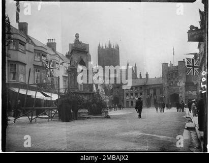 Market Place, Wells, Mendip, Somerset, 1907. Ein Blick nach Osten über den Market Place, vorbei am Market Cross, mit Fußgängern, die an Gebäuden mit Union-Jack-Flaggen und -Bändern vorbeilaufen. Stockfoto