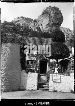 Lily Cottage, Cliff Road, Cheddar, Sedgemoor, Somerset, 1907. Mrs. Main steht im Vorgarten von Lily Cottage mit dem Haus hinter ihr und Lion Rock auf dem Hügel darüber. Im Negativindex für die Sammlung bezeichnet der Fotograf die Frau, die auf dem Foto als Frau Main dargestellt wird. Das ist wahrscheinlich Mrs. Charlotte Main, die Erfrischungsräume leitete, die im Kelly's Directory von Somerset, 1902, aufgeführt sind. Stockfoto