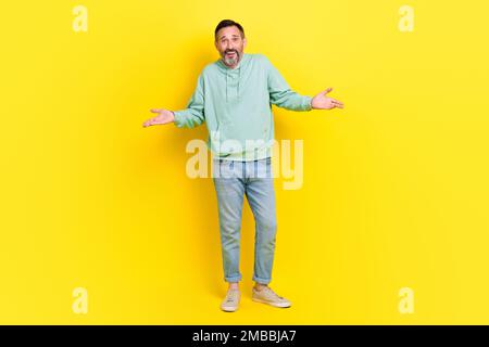 Ein Foto in voller Länge von einem flippigen Mann trägt trendige Kleidung hebt die Hände und zeigt keine Antwort, tut mir leid, steht leer, isoliert auf gelbem Hintergrund Stockfoto