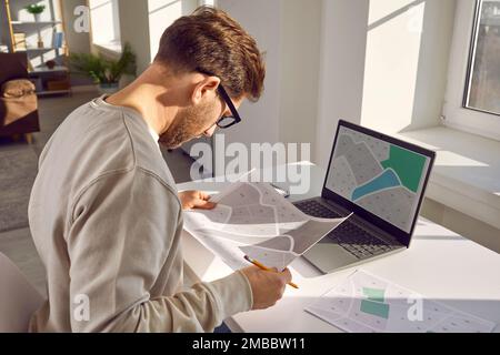 Professioneller Kartograf, der an seinem Arbeitsplatz mit einer gedruckten Katasterkarte arbeitet. Stockfoto