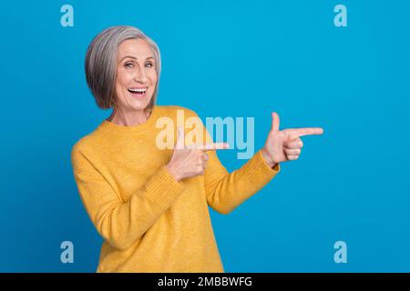 Fotoporträt einer reifen, reizenden Lady Finger zeigen leeren Raum kühle Geste elegant gelb aussehen isoliert auf blauem Hintergrund Stockfoto