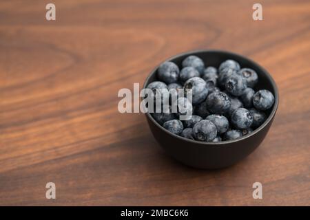 Große Bio-Heidelbeeren in einer schwarzen Schüssel auf Walnusstisch, flacher Fokus Stockfoto