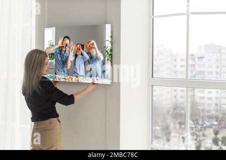 Leinwanddruck mit Gallery Wrap. Frau hängt Fotografie an der weißen Wand. Hände halten Fotoleinwand Druck Stockfoto