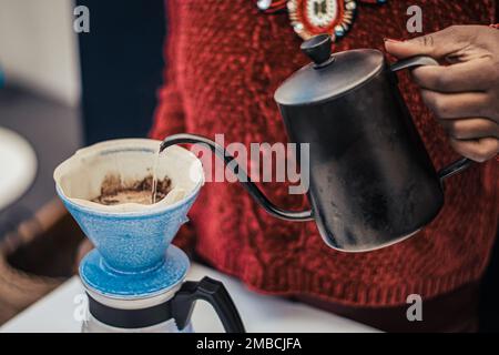 Schwarzes Hautmädchen, das schwarzen Kaffee mit einer Teekanne und einem Tuch oder einem Papierfilter zubereitet oder brüht Stockfoto