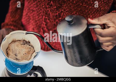 Schwarzes Hautmädchen, das schwarzen Kaffee mit einer Teekanne und einem Tuch oder einem Papierfilter zubereitet oder brüht Stockfoto