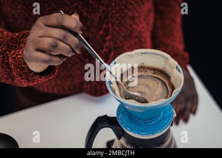 Schwarzes Hautmädchen, das schwarzen Kaffee mit einer Teekanne und einem Tuch oder einem Papierfilter zubereitet oder brüht Stockfoto