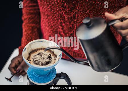 Schwarzes Hautmädchen, das schwarzen Kaffee mit einer Teekanne und einem Tuch oder einem Papierfilter zubereitet oder brüht Stockfoto