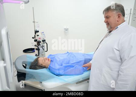 Der ältere Arzt hält die Hand des Patienten vor dem CT-Scan Stockfoto