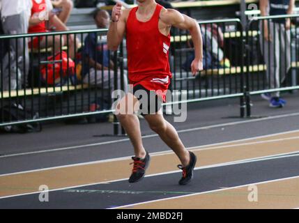 Ein männlicher High-School-Läufer, der während eines Leichtathletikrennens in roter Uniform auf einer Hallenbahn sprint. Stockfoto