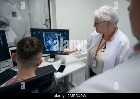 Kollegen Diagnostiker, eine ältere Frau und Männer, führen eine MRT-Untersuchung durch Stockfoto